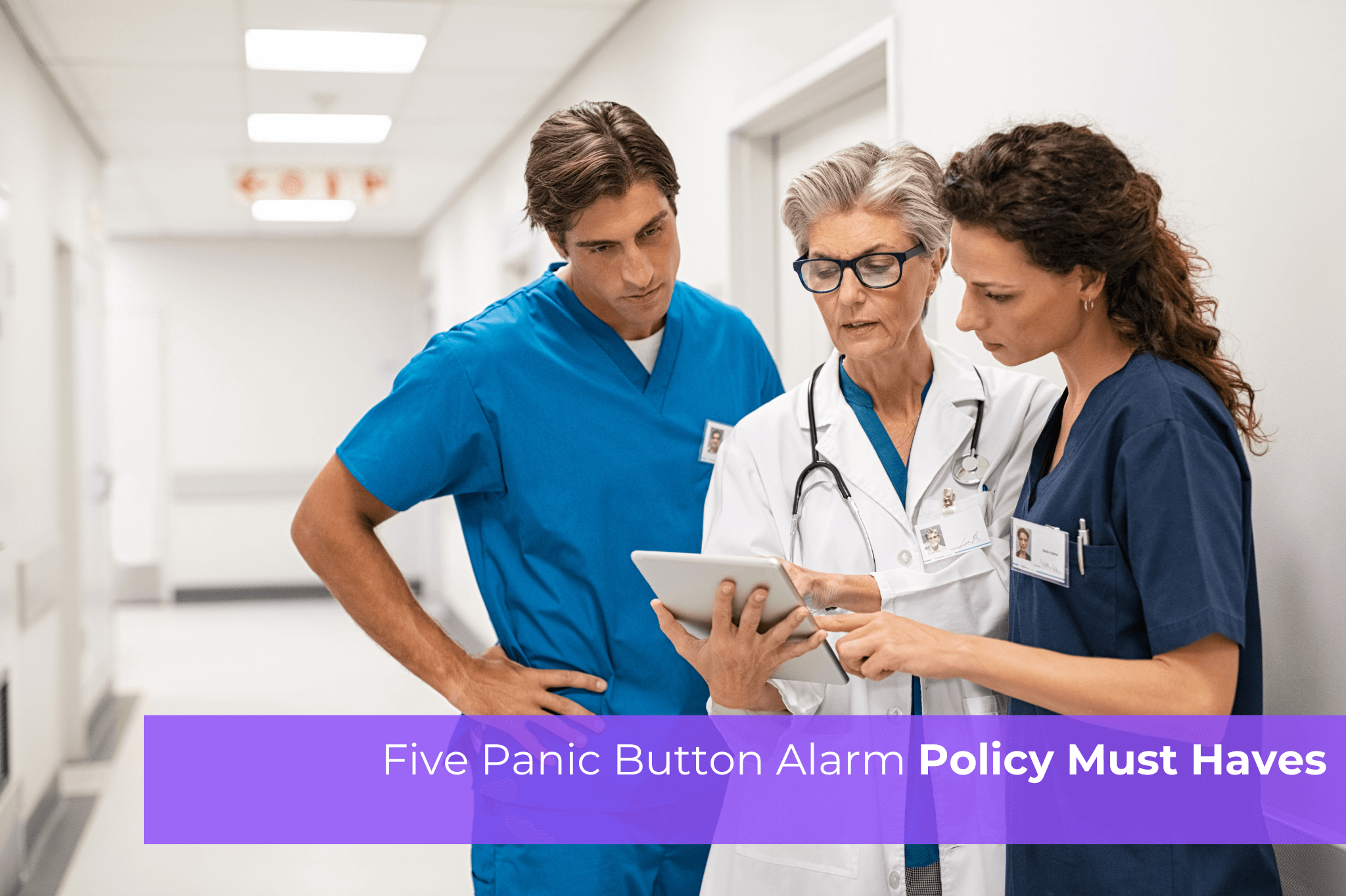 Three healthcare workers in scrubs and a lab coat reviewing information together on a tablet in a hospital hallway.
