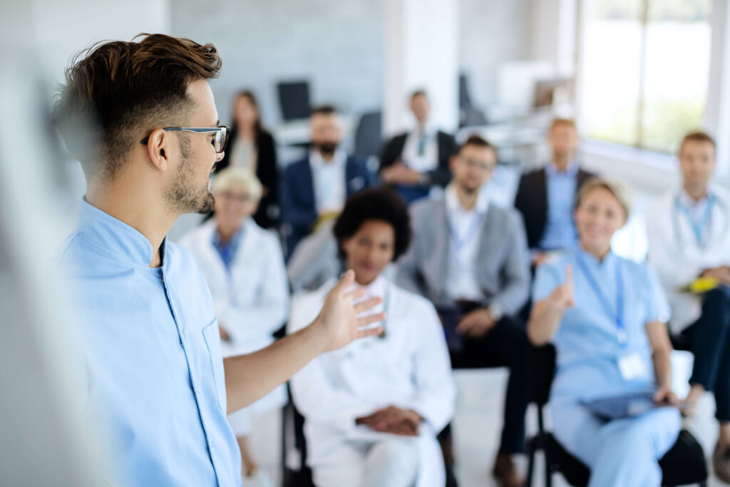 Speaker presenting to a seated audience of healthcare professionals in a training session