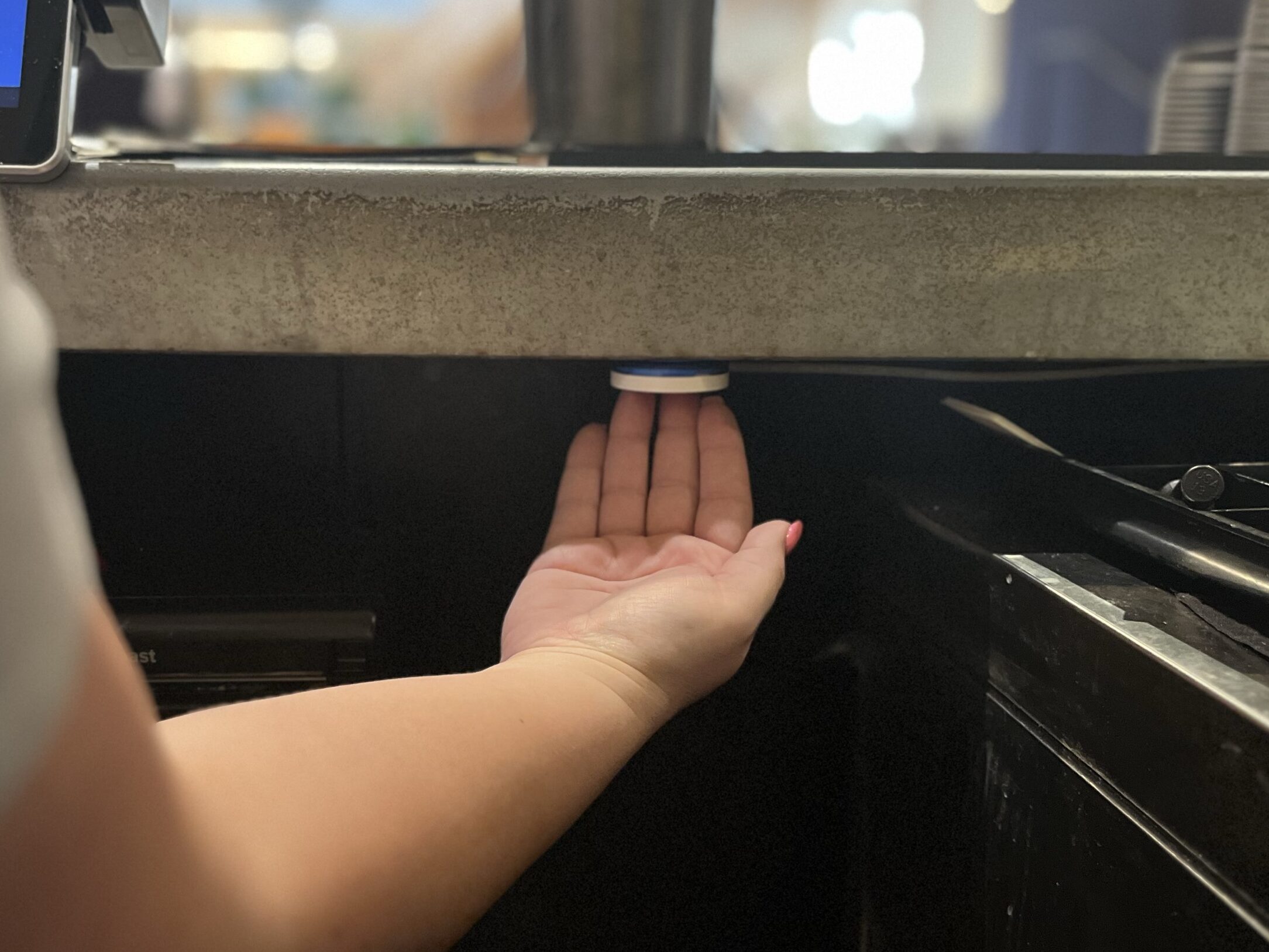 Hand reaching under a counter to press a ROAR under-desk panic button