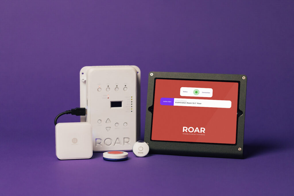 ROAR safety system components arranged against a purple background: base unit, hub, panic button, and a tablet display showing the ROAR interface.