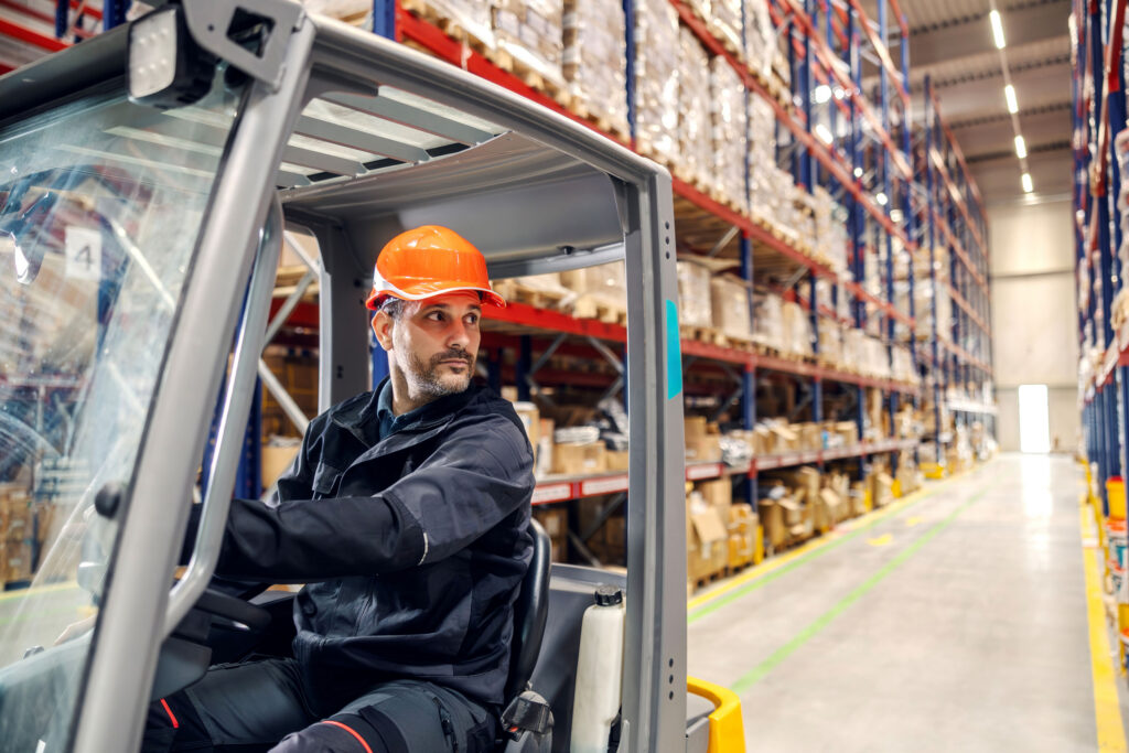 Warehouse worker in an orange hard hat operating a forklift.