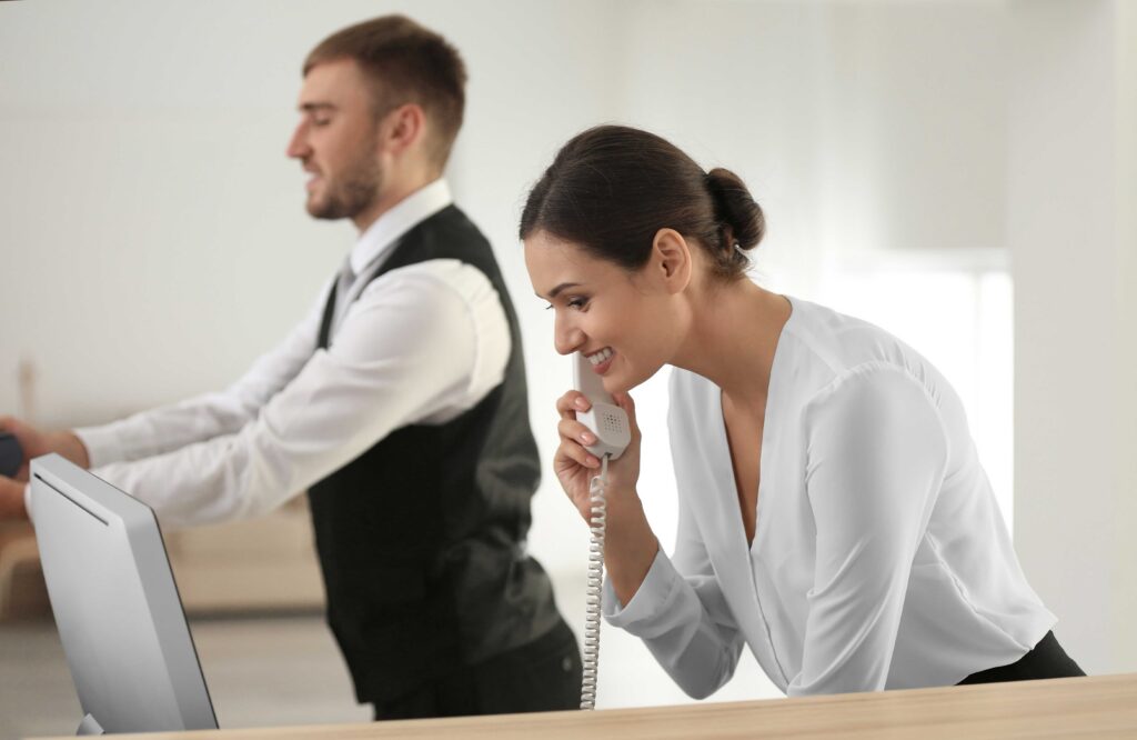 female hospitality worker at the hotel's front desk taking a call, male worker behind her leaning into counter