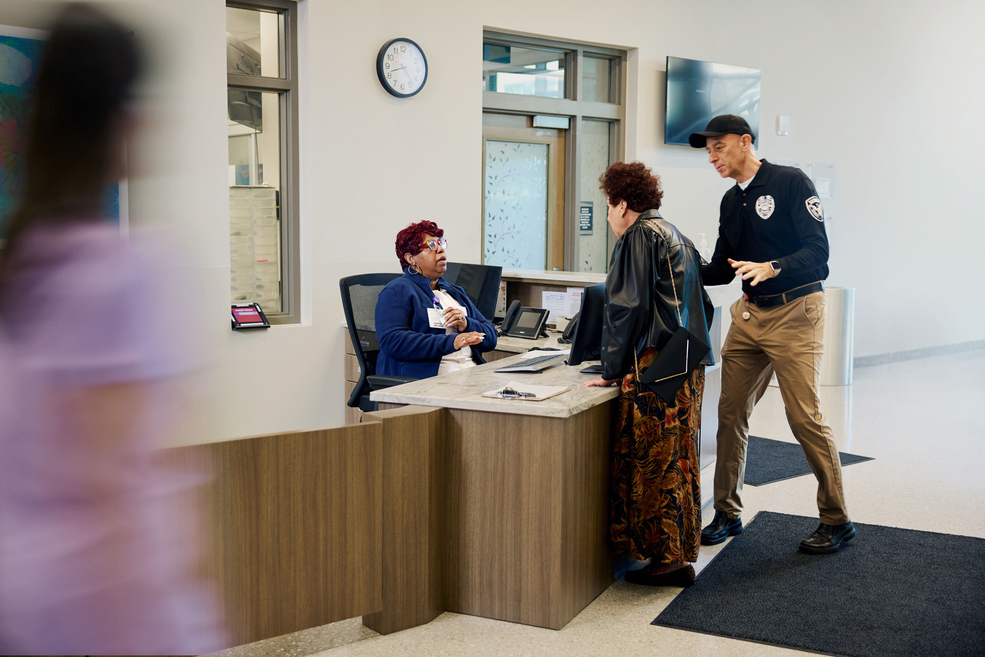 healthcare reception desk with receptionist, guest, security guard and blurry medical staff entering photo frame