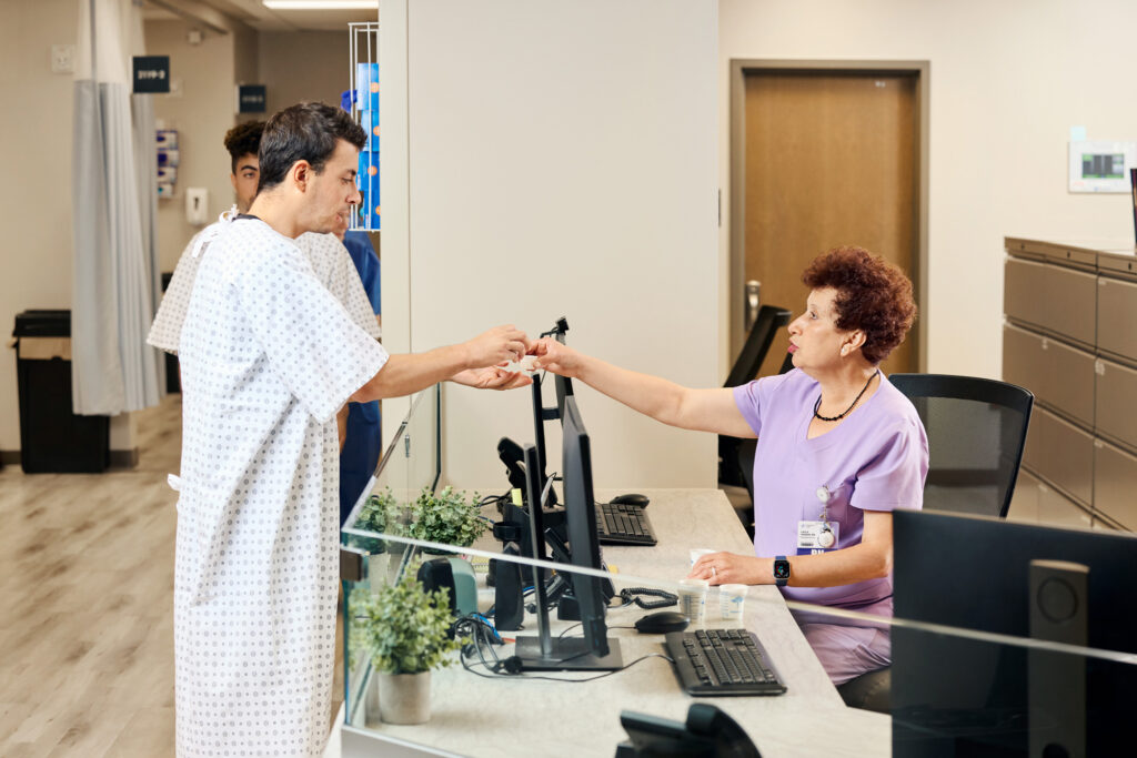 patient in medication line taking medicine from a nurse seated at a desk